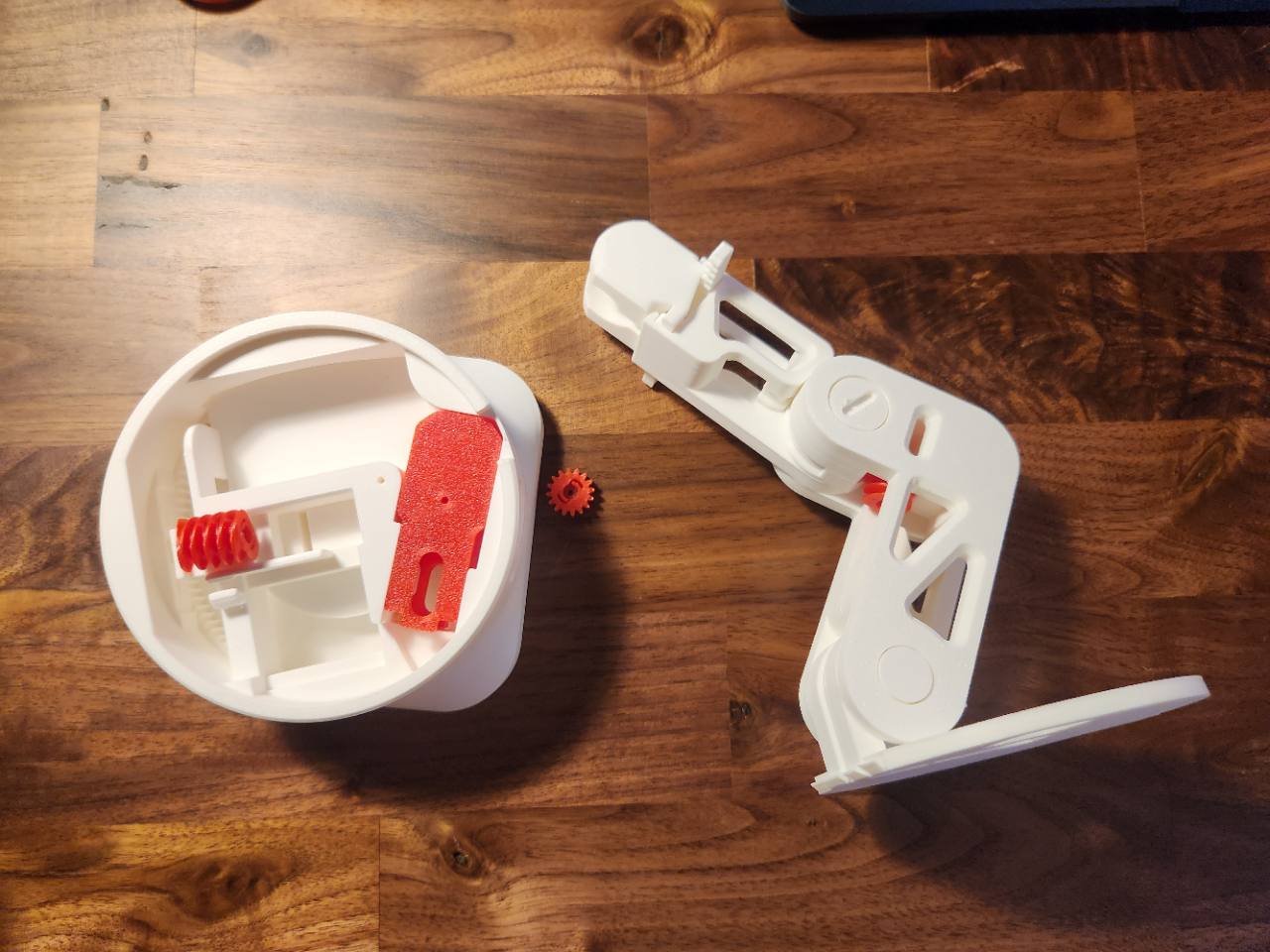 Disassembled white and red 3D-printed mechanism parts on a wooden table